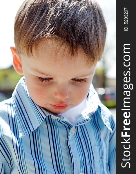 Close-up shot of a young boy looking down wearing a blue button-up shirt.