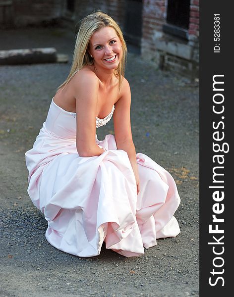 Vertically framed outdoor shot a smiling attractive bridesmaid crouching down in unpaved lot. Vertically framed outdoor shot a smiling attractive bridesmaid crouching down in unpaved lot.