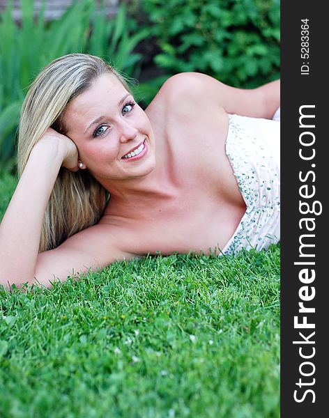 Attractive blond woman in a bridesmaid's dress lying on a lush green lawn propping her head up on her hand. Vertically framed shot. Attractive blond woman in a bridesmaid's dress lying on a lush green lawn propping her head up on her hand. Vertically framed shot.