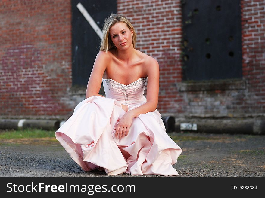 Horizontally framed outdoor shot of an attractive bridesmaid crouching down in front of red brick wall. Horizontally framed outdoor shot of an attractive bridesmaid crouching down in front of red brick wall.