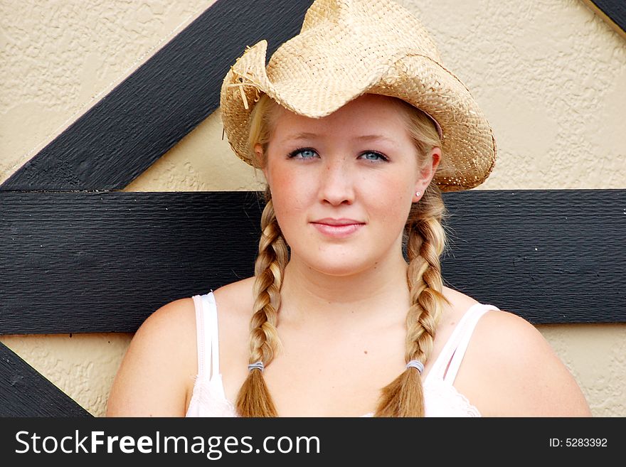 Horizontally framed outdoor shot of a smiling teenage girl, with blond hair and blue eyes, standing next to barn door wearing a straw cowboy hat. Horizontally framed outdoor shot of a smiling teenage girl, with blond hair and blue eyes, standing next to barn door wearing a straw cowboy hat.