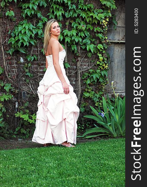 Attractive blond woman in a bridesmaid's dress standing on a lush green lawn. Attractive blond woman in a bridesmaid's dress standing on a lush green lawn