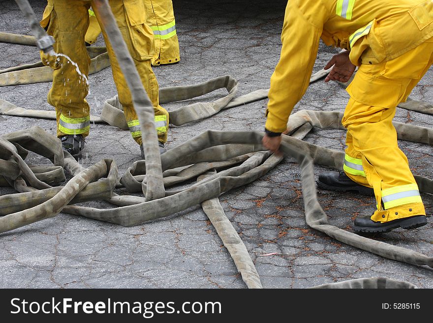 Fire-fighters picking up hoses after fire training. Fire-fighters picking up hoses after fire training