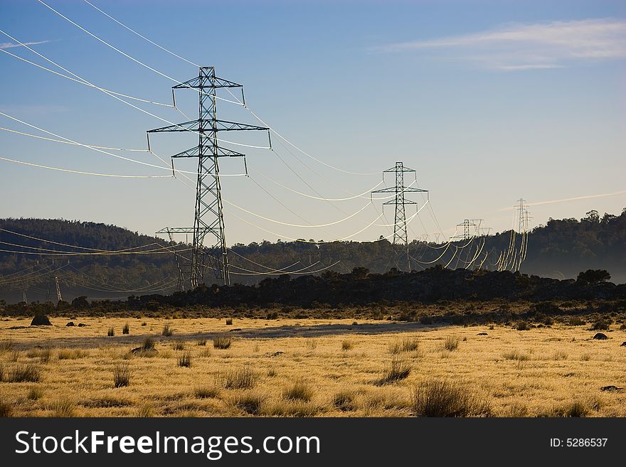 Power pylons and powerlines crossing farmland with dry grass in the forground