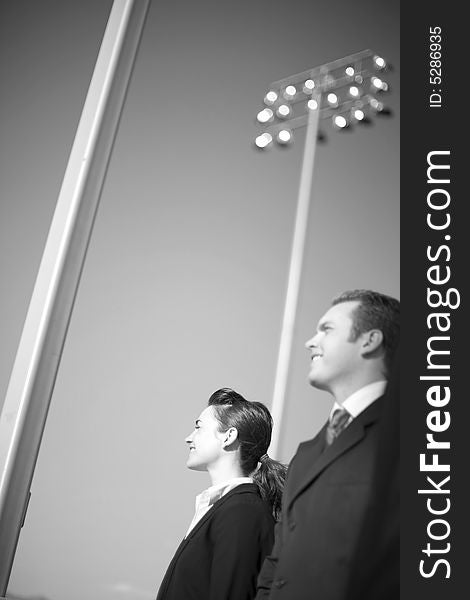 Profile view of businessman and businesswoman standing in formal wear in front of large lights. Profile view of businessman and businesswoman standing in formal wear in front of large lights