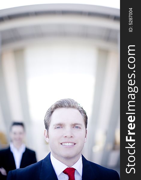 Attractive young businessman with businesswoman in background standing in front of building. Attractive young businessman with businesswoman in background standing in front of building