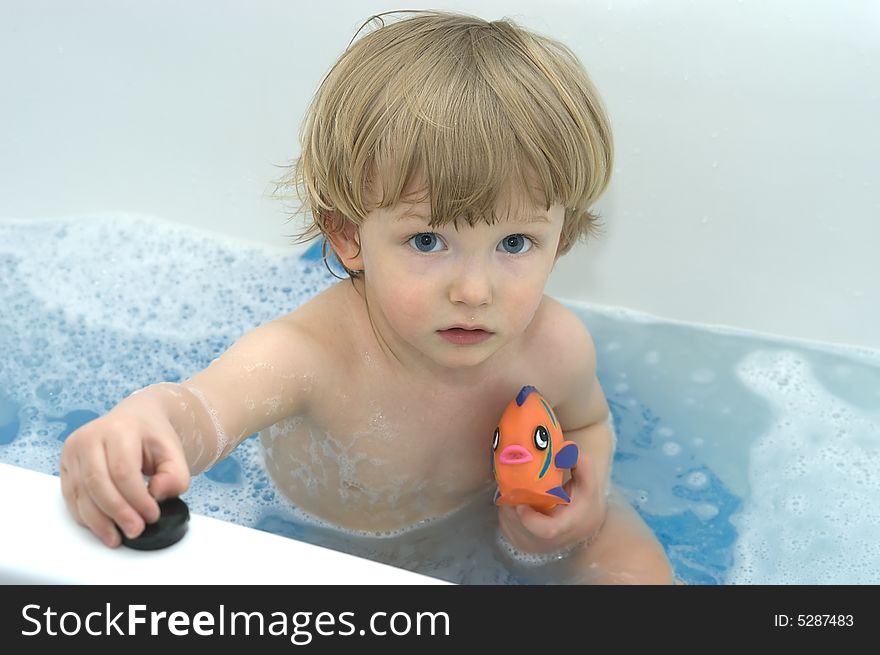 Pensive boy in bath mit toy fish