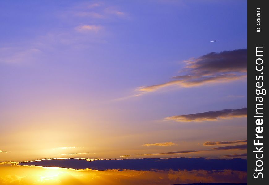 Backlit cloudscape featuring a orange and purple sky.