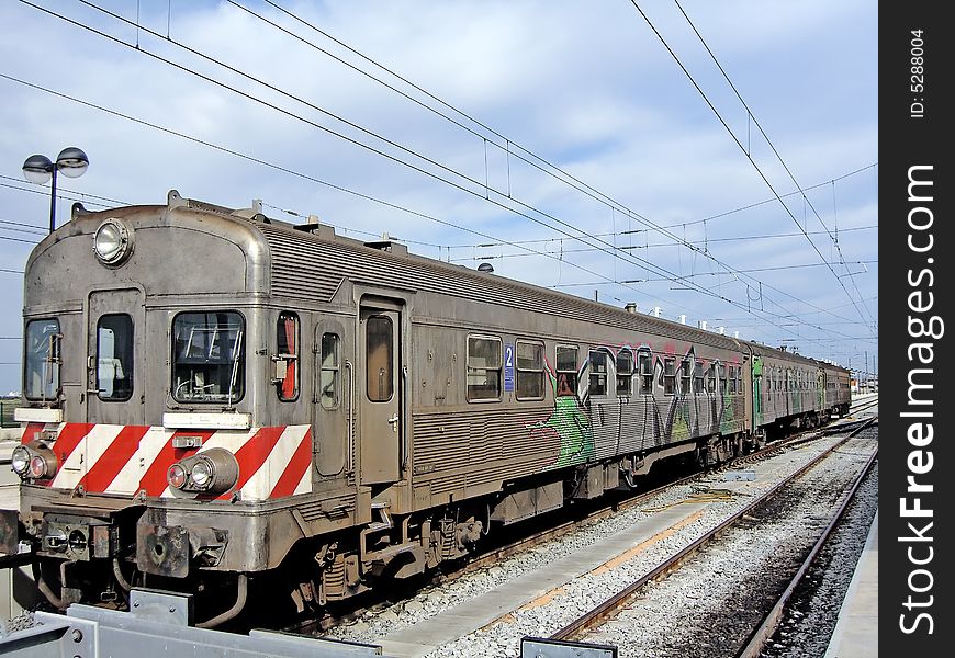 View of a portuguese train parked in a train station with some painted graffitti.