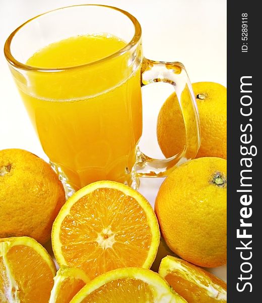 Glass of orange juice with some oranges surrounding it isolated on a white background.