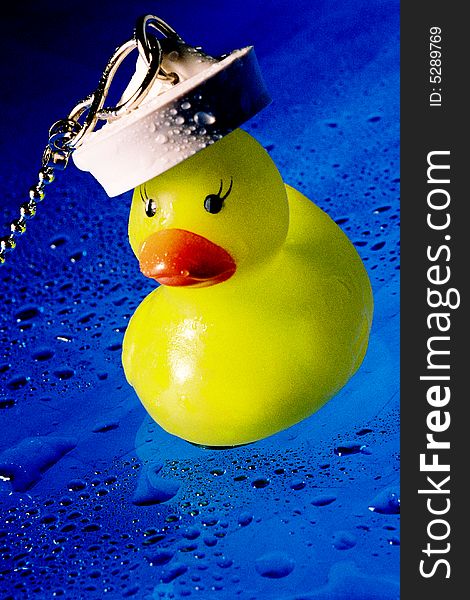 A colourful image of a rubber duck with a bath plug on his head that makes him look like a sailor ducky. the background is blue and is covered with little droplets