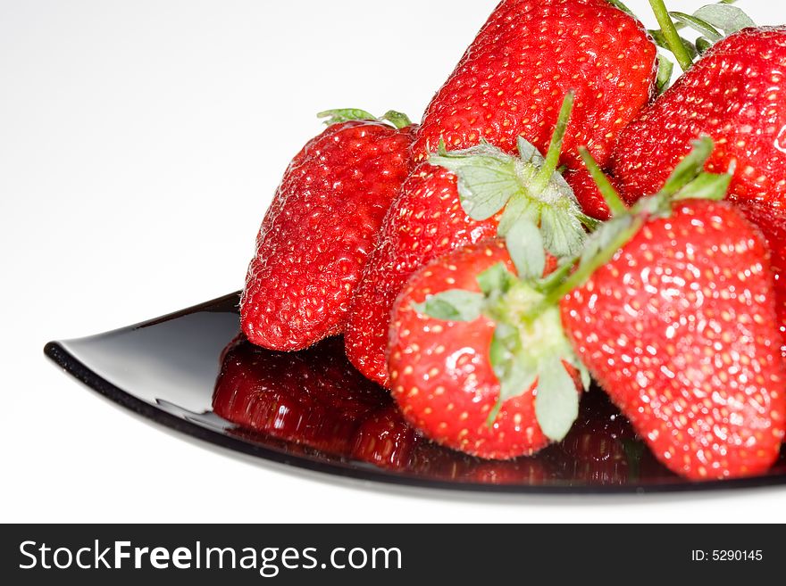 Fresh red strawberries on black plate isolated on white