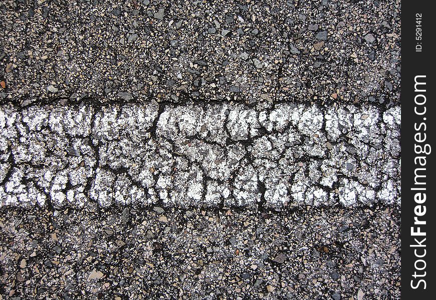 Straight white line view of an asphalt road with many cracks.