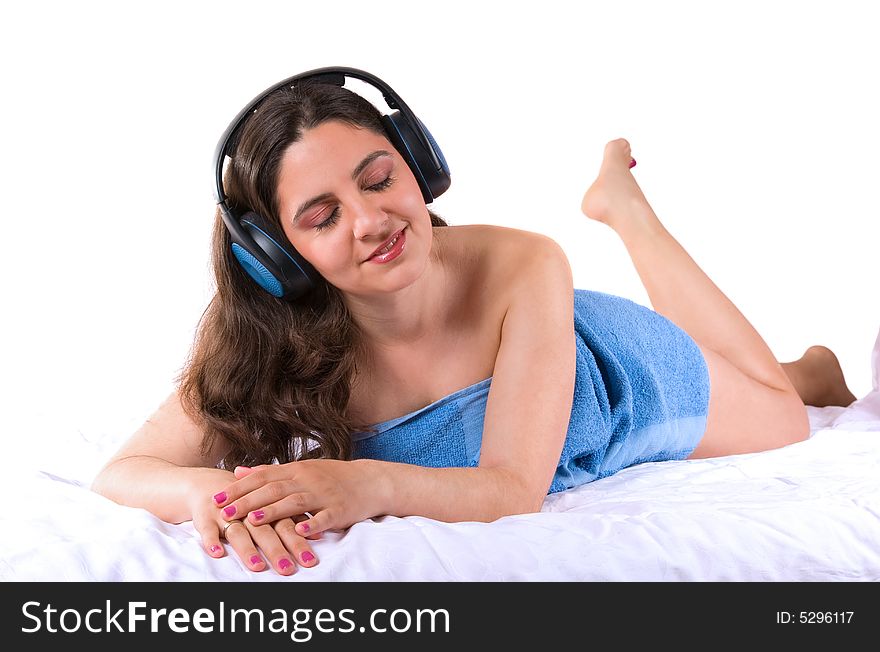 A beautiful girl, lying wrapped in a blue towel, wearing headphones, enjoying the music, with her eyes closed. A beautiful girl, lying wrapped in a blue towel, wearing headphones, enjoying the music, with her eyes closed