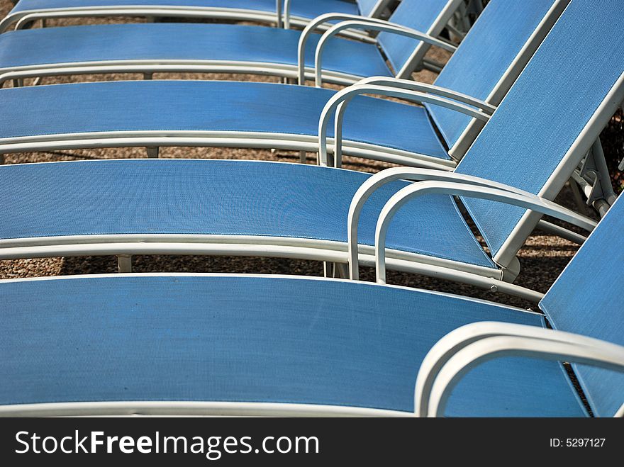 Row of blue chaise lounges by a pool.