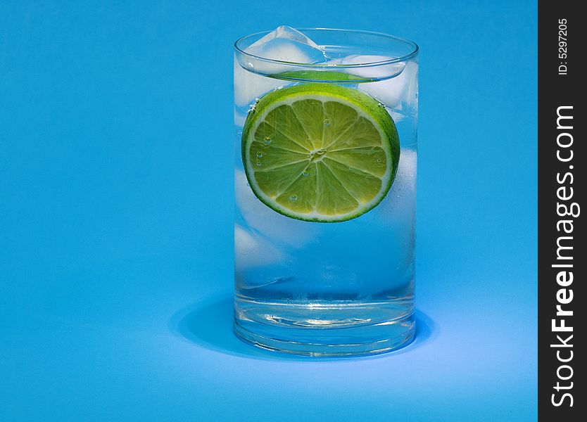 Glass of lime drink with ice cubes on blue background. Glass of lime drink with ice cubes on blue background.