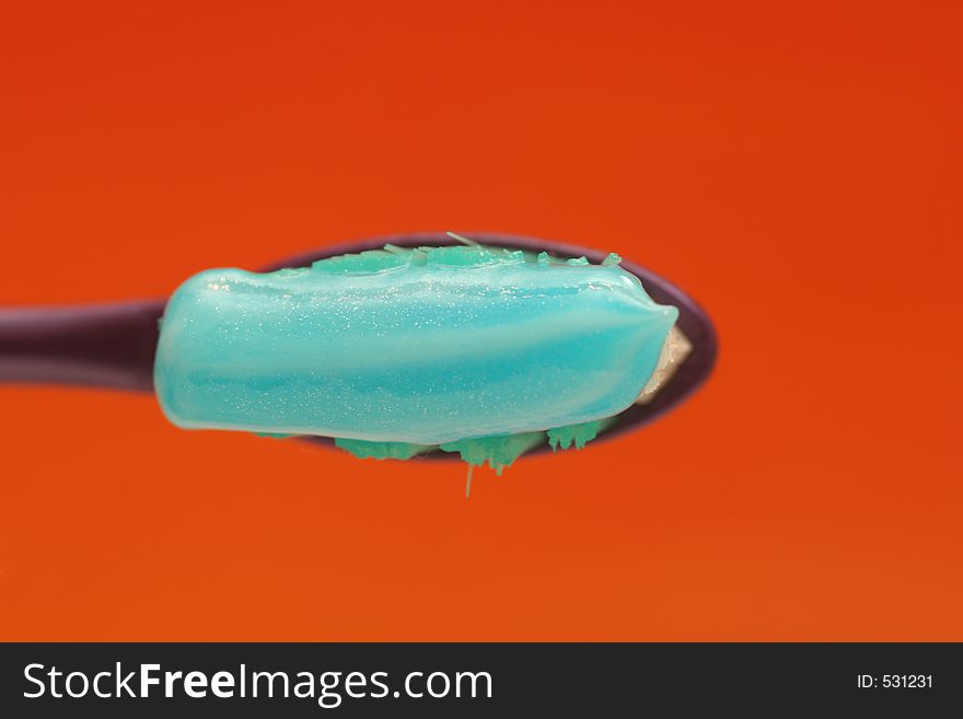 Toothbrush with toothpaste isolated on orange background shown from top. Toothbrush with toothpaste isolated on orange background shown from top