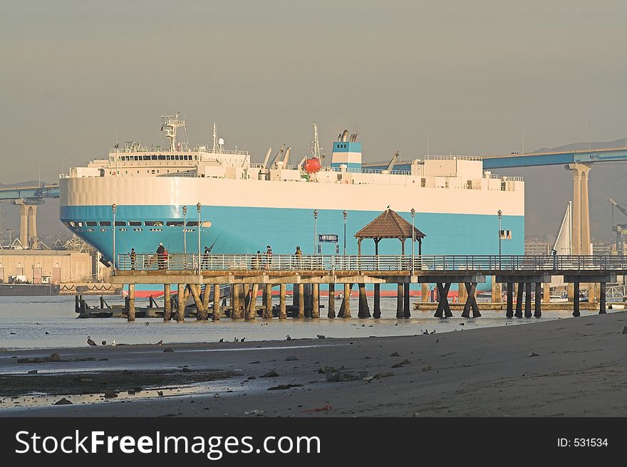 Cargo ship leaves Port of San Diego bound for Japan. Coronado ferry landing with young kids fishing in the midground.