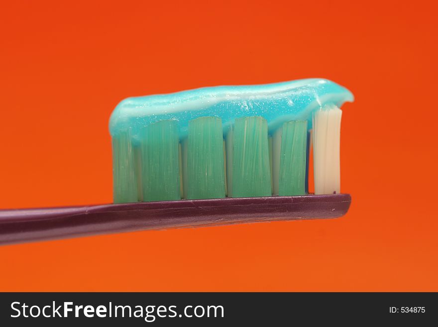 Macro of a toothbrush with toothpaste against orange background