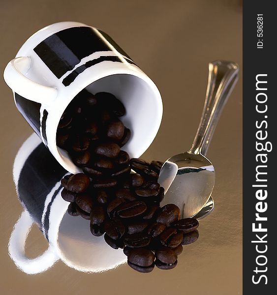 An espresso cup with roasted coffee beans and a small silver spoon. An espresso cup with roasted coffee beans and a small silver spoon
