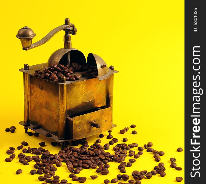 Antiquity coffee machine with beans over yellow background