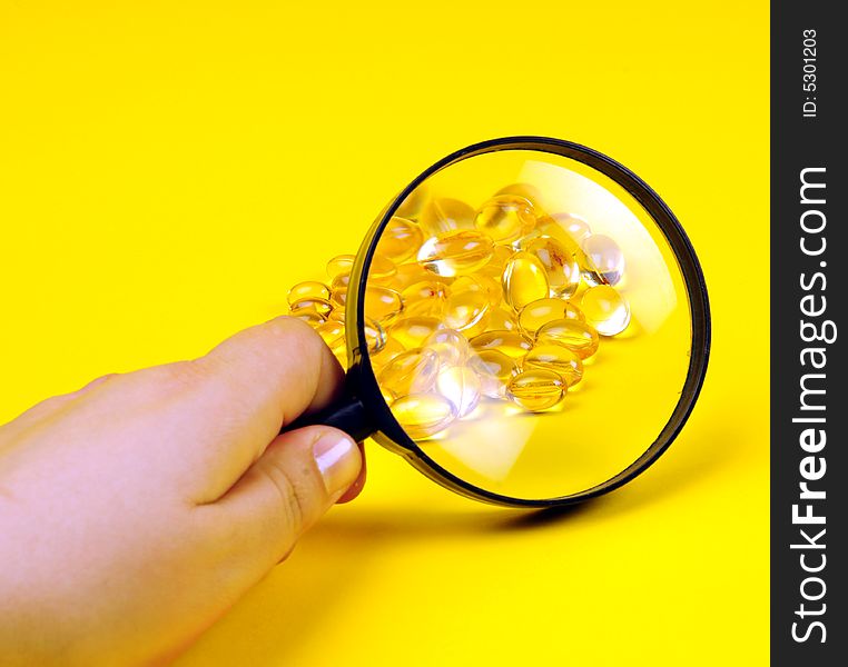 A view with some vitamins and magnifying glass over yellow background