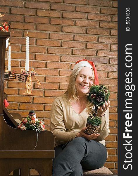 A women holding a Christmas decoration sitting by a piano with Christmas candles. A women holding a Christmas decoration sitting by a piano with Christmas candles.