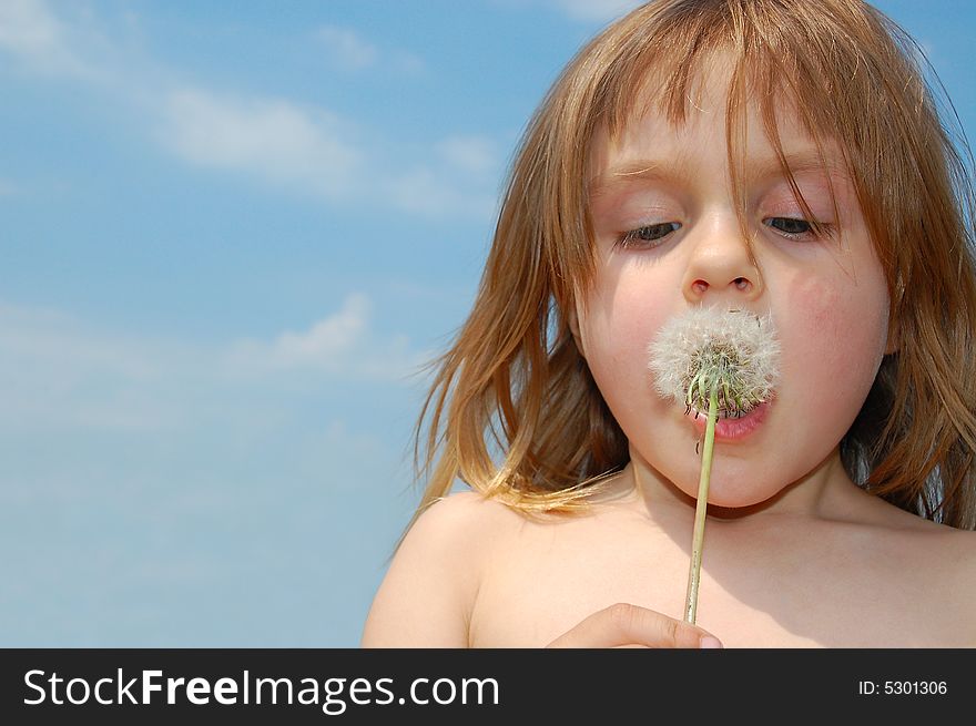 Little girl blowing a dandelion on the blue sky background