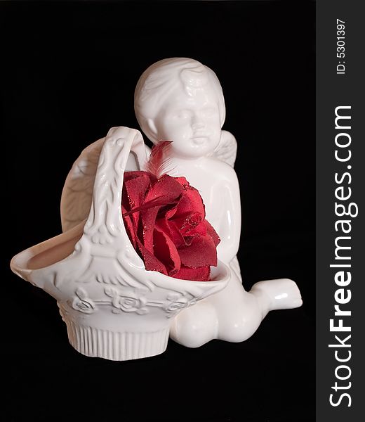 Love gift with ceramic angel figure and red artificial rose isolated on black. Love gift with ceramic angel figure and red artificial rose isolated on black