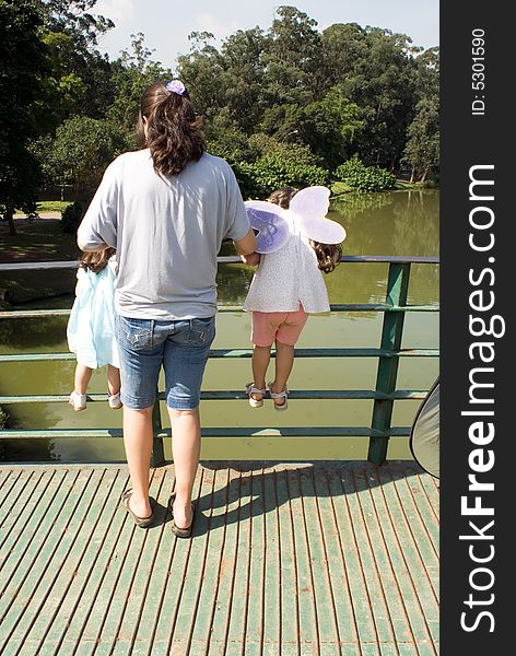 Mother and her two daughters looking over the railing of a bridge on a sunny day. Vertically framed shot. Mother and her two daughters looking over the railing of a bridge on a sunny day. Vertically framed shot.