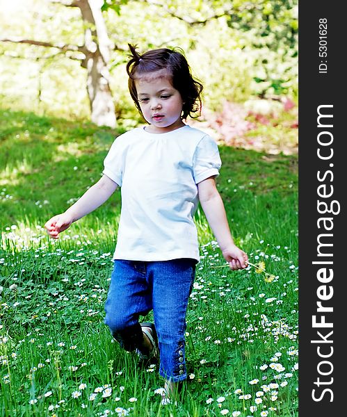 Cute little girl picking summer flowers on a sunny day in the park. Vertically framed shot.