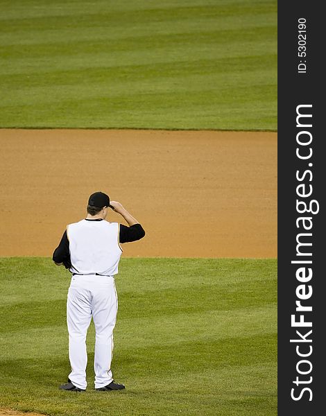 Baseball pitcher standing in the infield holding his hat. Baseball pitcher standing in the infield holding his hat