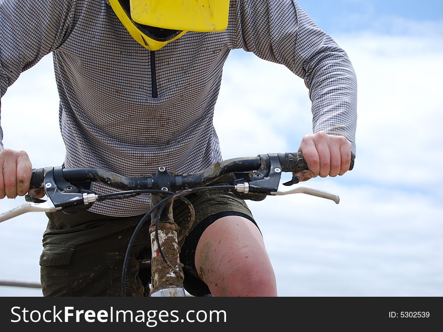 Mud-splattered mountain biker against a dirt road and green pasture. Mud-splattered mountain biker against a dirt road and green pasture.