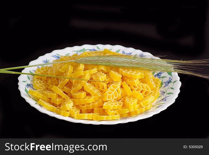 Plate with the macaronis and the ear of wheat against the black background. Plate with the macaronis and the ear of wheat against the black background