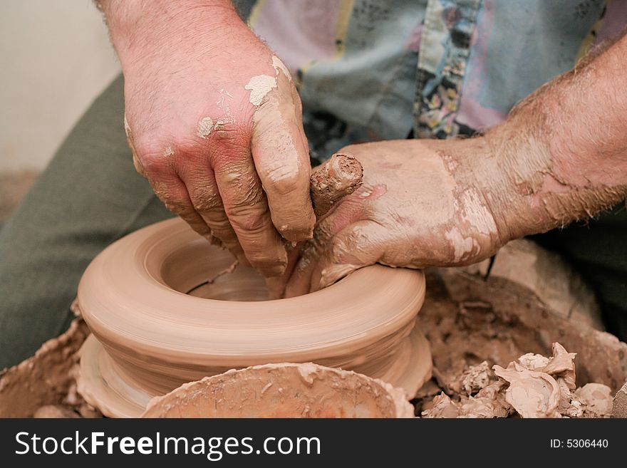 Overworked hands. Artist shaping a bowl on a pottery wheel. Shallow depth of field with focus on the fingers. Motion blur on the spinning bowl and wheel. Overworked hands. Artist shaping a bowl on a pottery wheel. Shallow depth of field with focus on the fingers. Motion blur on the spinning bowl and wheel.
