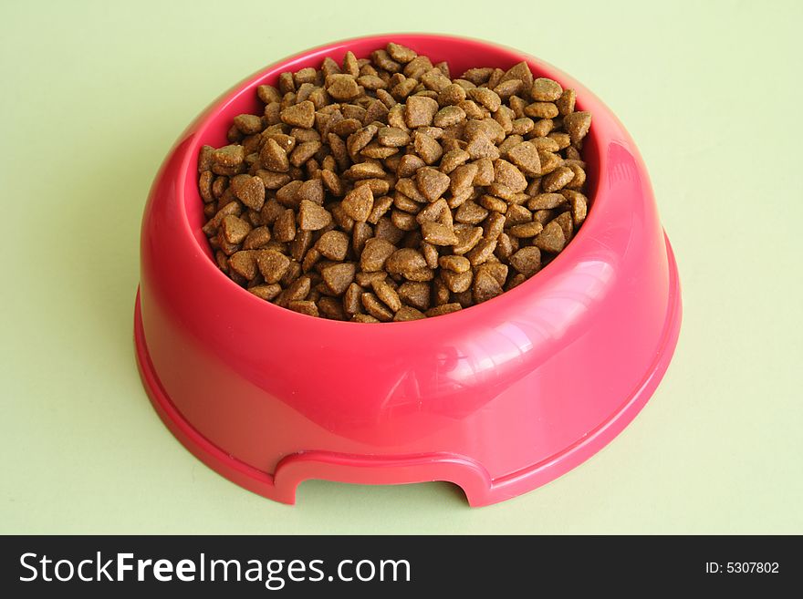 Pink dog bowl full of biscuits over green background. Pink dog bowl full of biscuits over green background