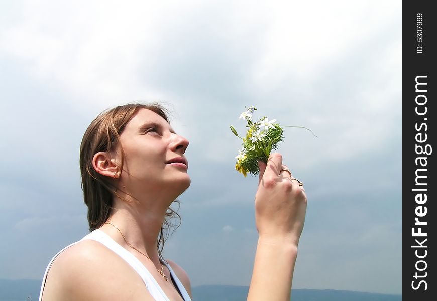 Beautiful girl smelling wild flowers with summer storm clouds behind