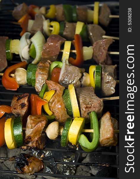 Several Shishkabobs lined up  cooking on a grill