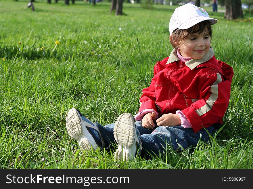 Little girl in the park sitting on green grass