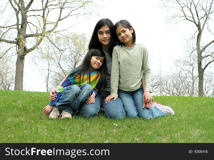 Three sisters sitting on grassy hilltop. Part Scandinavian, Thai heritage.