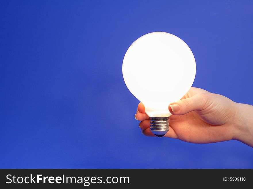 Female hand holding glowing light bulb on a blue background.