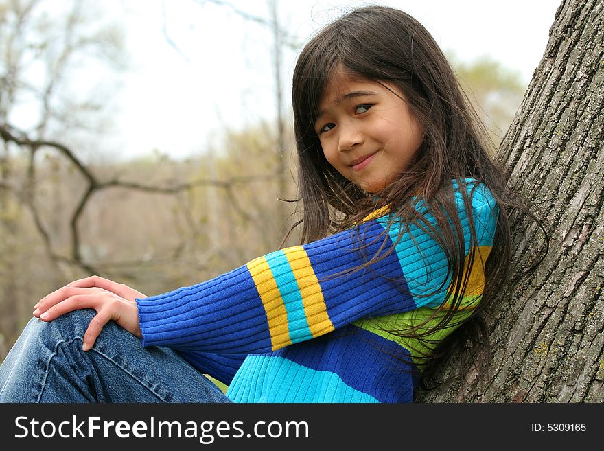 Adorable little girl sitting against  tree