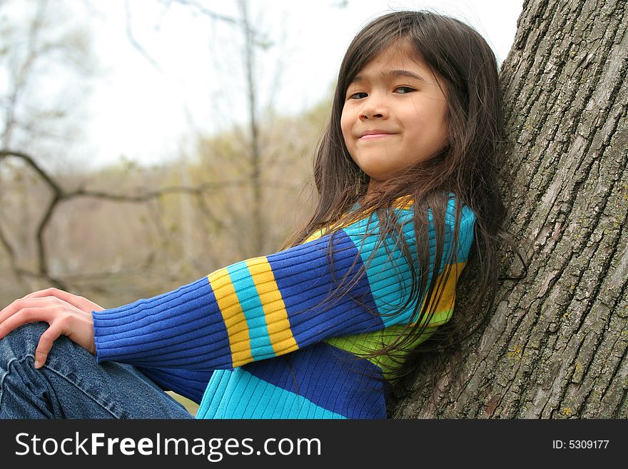 Adorable little girl sitting against  tree