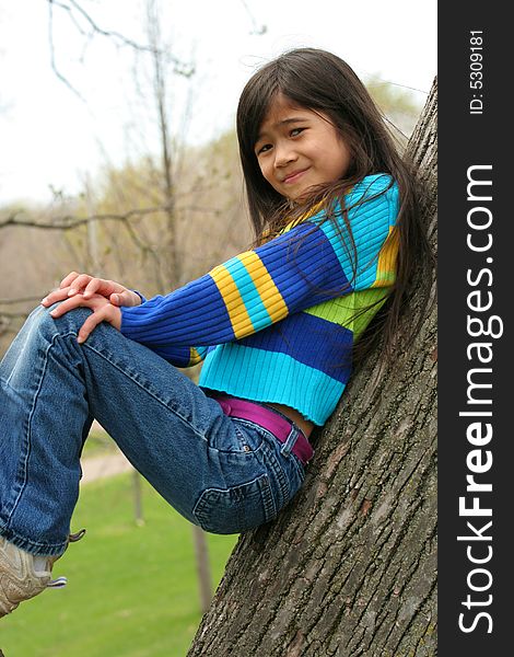 Adorable little girl sitting against  tree