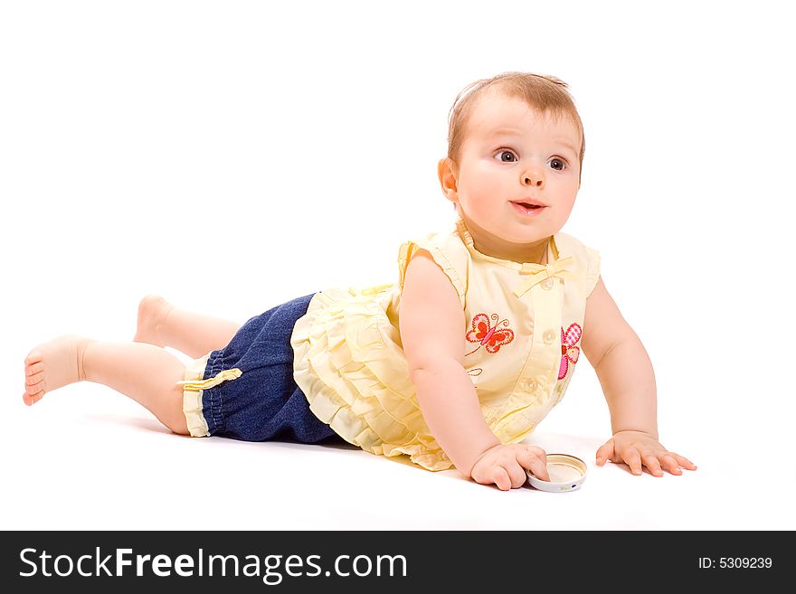 Pretty  smiling baby in suit from summer blouse and jeanse shorts lying on belly and hold in hand a cap from child`s food jar. Pretty  smiling baby in suit from summer blouse and jeanse shorts lying on belly and hold in hand a cap from child`s food jar
