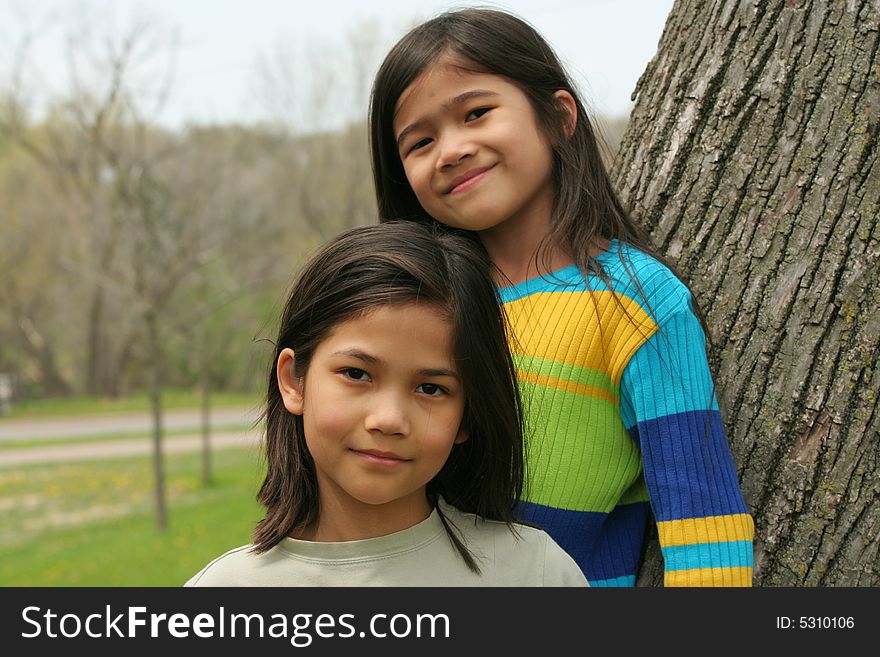 Two little girls standing against tree in spring. Two little girls standing against tree in spring