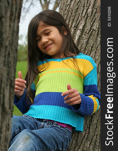 Adorable little girl sitting up against tree. Part Asian,Scandinavian descent