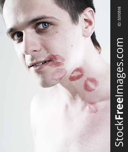 Red kisses on face of young man at white background