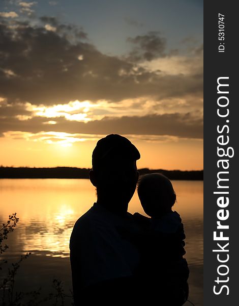 Silhouette portrait of a Father holding his young Daughter on the shore of a lake at sunset. Silhouette portrait of a Father holding his young Daughter on the shore of a lake at sunset