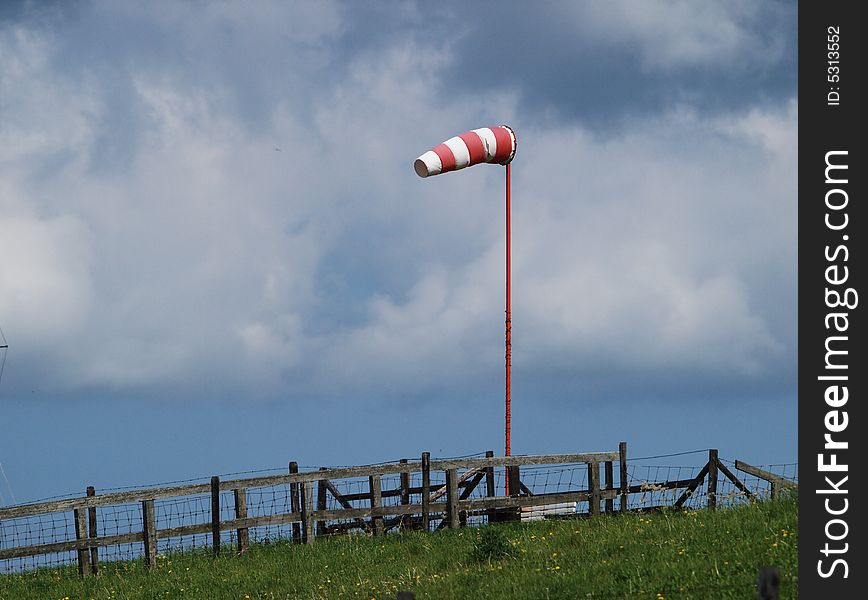 Red and white windsock on a dike with grass in a sky with clouds